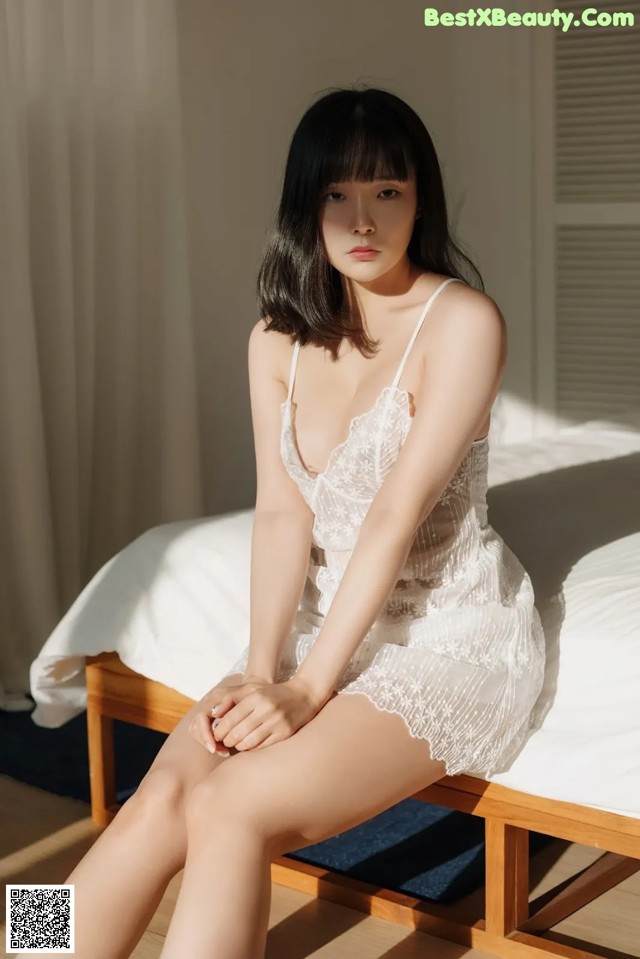 A woman sitting on top of a bed in a white dress.