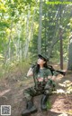 A woman in a military uniform holding a rifle in the woods.