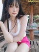 A woman sitting on a wooden bench under an umbrella.