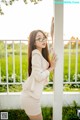 A woman in a white suit leaning against a white pole.