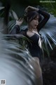 A woman in a black bodysuit posing in front of a palm tree.