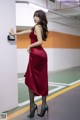 A woman in a red dress leaning against a wall.