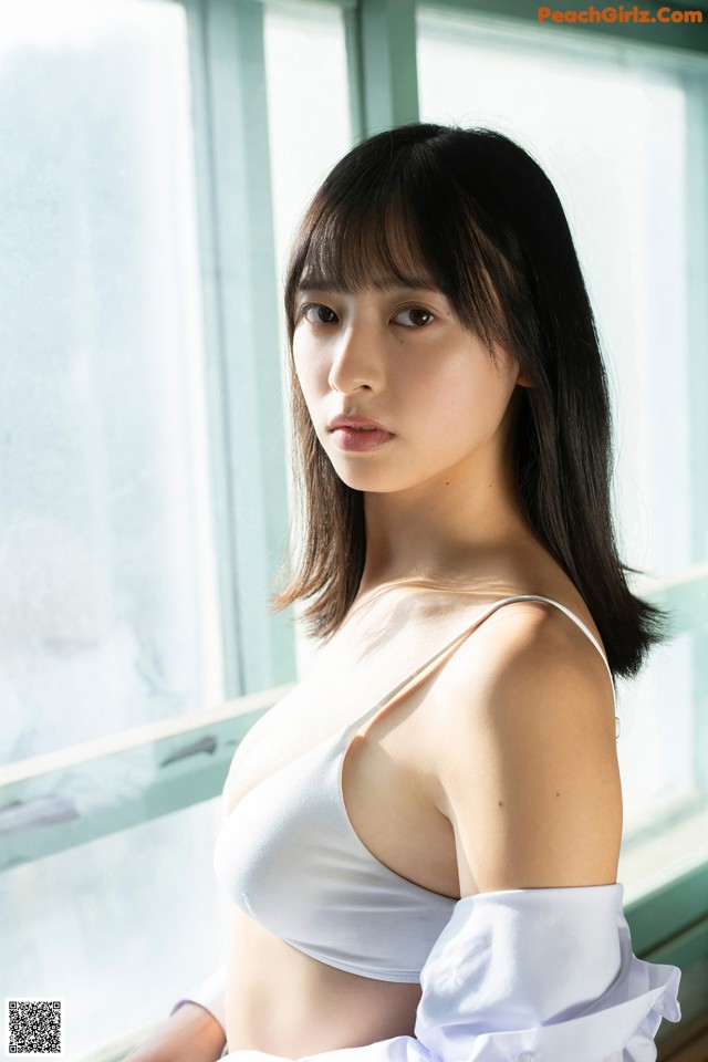 A woman in a white shirt is posing by a window.
