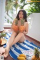 A woman sitting on a towel holding two pineapples.