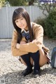 A young woman in a school uniform crouching on the ground.