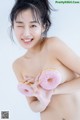 A naked woman holding two pink donuts in her hands.