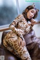 A woman in a leopard print catsuit sitting on a brown couch.