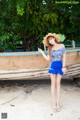 A woman in a blue dress and hat standing next to a boat.