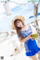 A woman in a blue dress and straw hat holding a coconut.