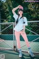 A woman in a white shirt and pink pants posing on a tennis court.