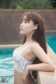 A woman in a white bra and panties leaning against a wall by a pool.