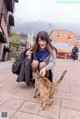 A woman crouches down to pet a cat on the street.