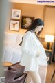 a woman in a white suit standing in front of a bed