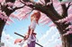 A woman with red hair stands under cherry blossoms, holding a sword.