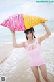 A woman in a pink bathing suit holding an ice cream cone on the beach.