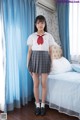 A woman in a school uniform standing in front of a bed.