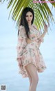 A woman in a pink dress standing next to a palm tree.