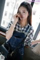 A woman wearing overalls and a plaid shirt is looking out a window.