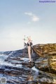 A woman standing on a rocky beach holding a sword.