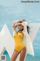 A woman in a yellow swimsuit posing on the beach.