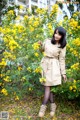 A woman standing in front of a bush of yellow flowers.