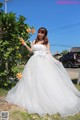 A woman in a wedding dress standing in front of a tree.