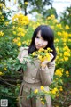 A woman standing in front of a bush of yellow flowers.