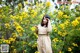 A woman standing in front of a bush of yellow flowers.