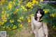 A woman sitting in front of a bush of yellow flowers.