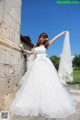 A woman in a wedding dress leaning against a stone wall.